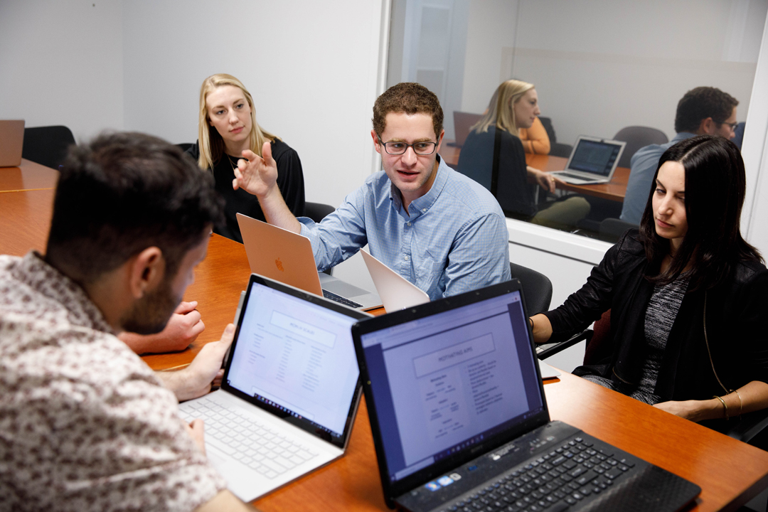 four students with laptops open in discussion at a conference table