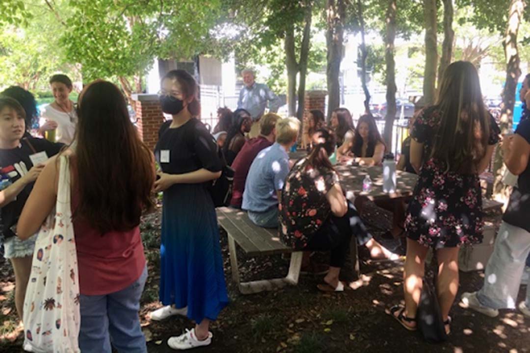 Students gathering outside at a picnic table with food, wearing masks